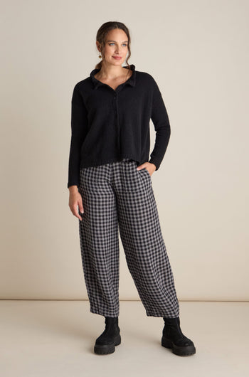 A person stands against a plain background wearing a black sweater and Linen Check Trousers with an elasticated waist, paired with black boots.