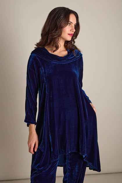 A person wearing a flowing Cowl Silk Velvet Dress in blue stands against a plain background.