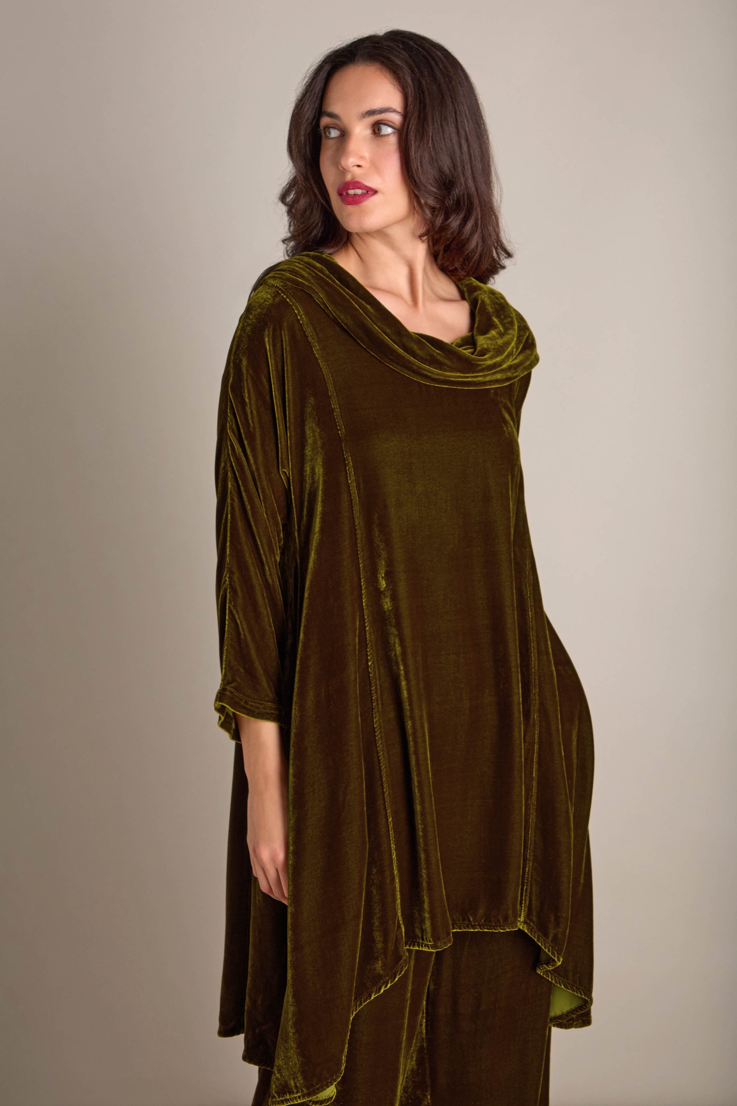 A person wearing a loose-fitting, olive-green silk velvet outfit reminiscent of the Cowl Silk Velvet Dress stands against a neutral background, looking to the side.