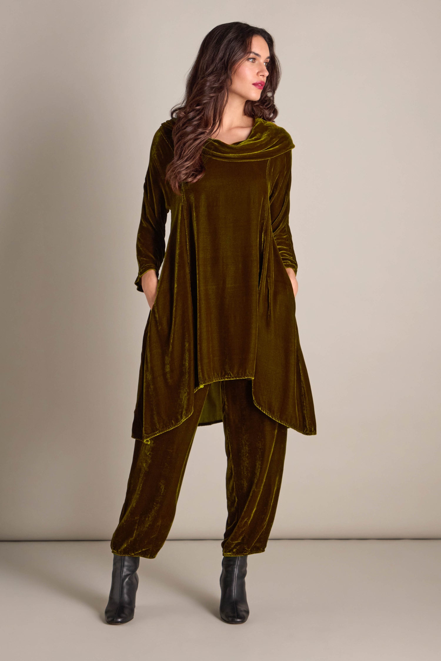 A person stands against a plain background in a Cowl Silk Velvet Dress featuring loose-fitting long sleeves and relaxed pockets.