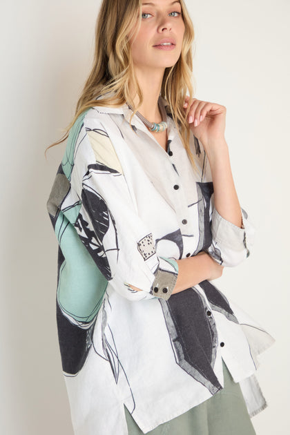 Woman wearing a long-sleeved, oversized Surreal Collage Print Linen Shirt by Grizas featuring abstract black, green, and beige patterns, standing against a plain background.