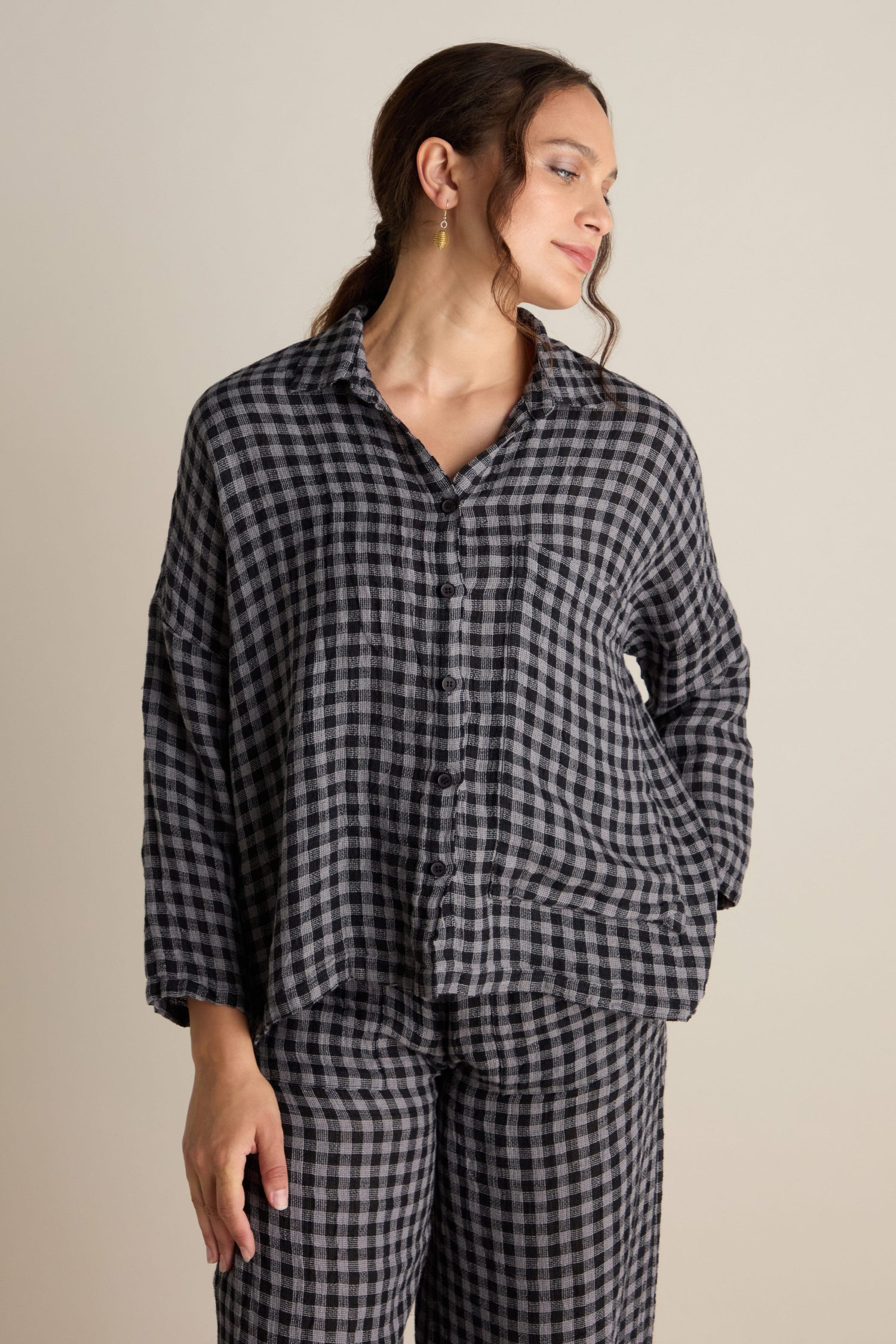 A person wearing the Linen Check Big Pocket Shirt in black and white checkered long-sleeve linen, paired with matching pants, stands against a plain background.