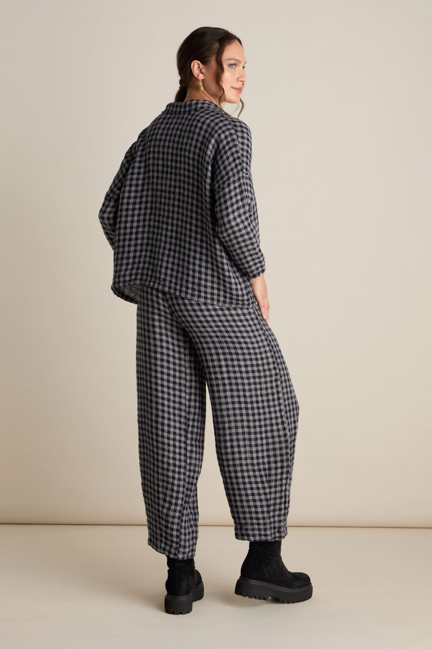 A person is standing sideways wearing a loose-fitting Linen Check Big Pocket Shirt in grey and black, paired with black platform shoes, perfect for day-dressing.