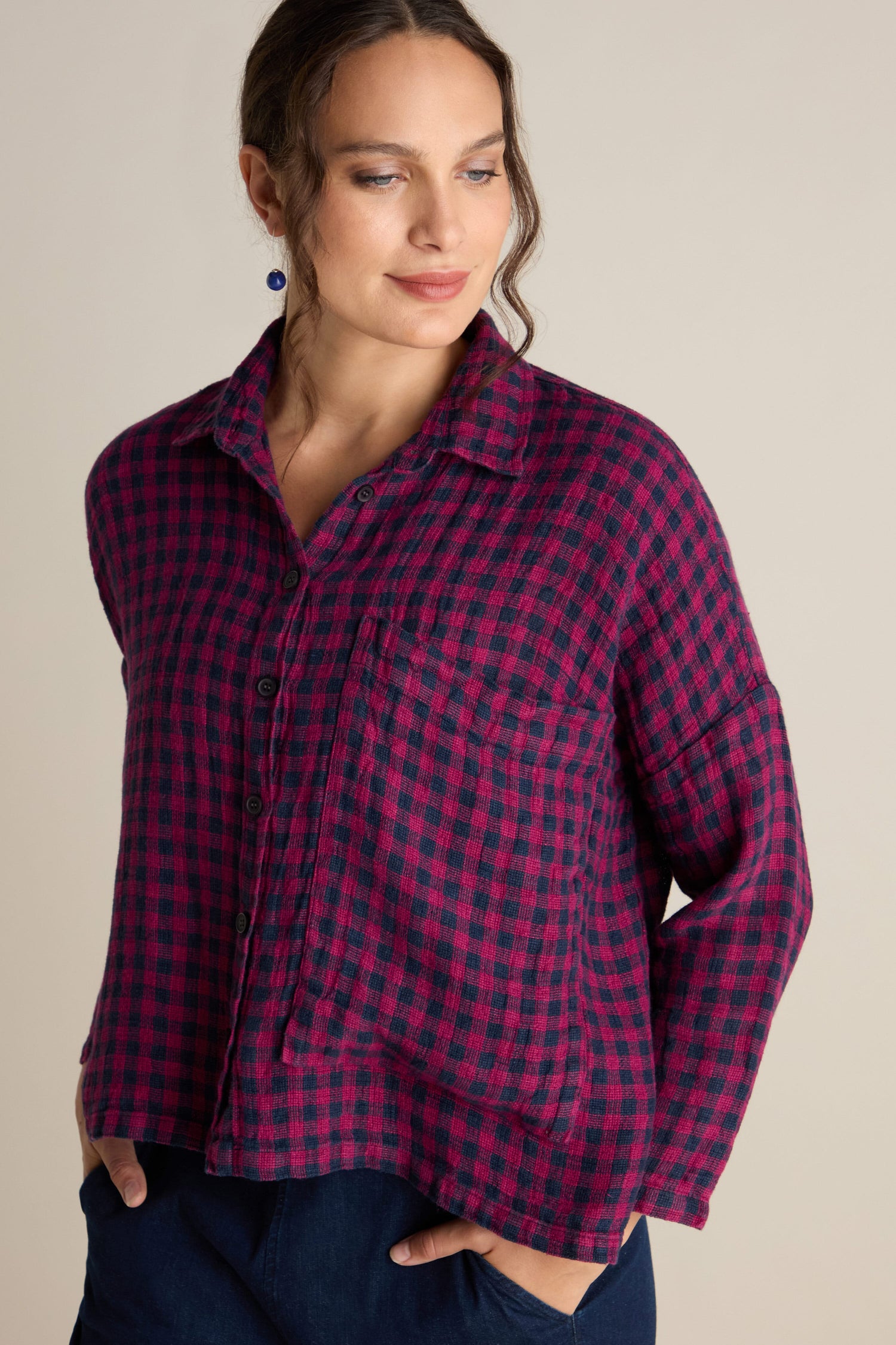 A person wearing the Linen Check Big Pocket Shirt in red and navy plaid with blue pants, featuring an oversized pocket, looking to the side. Perfect for day-dressing.