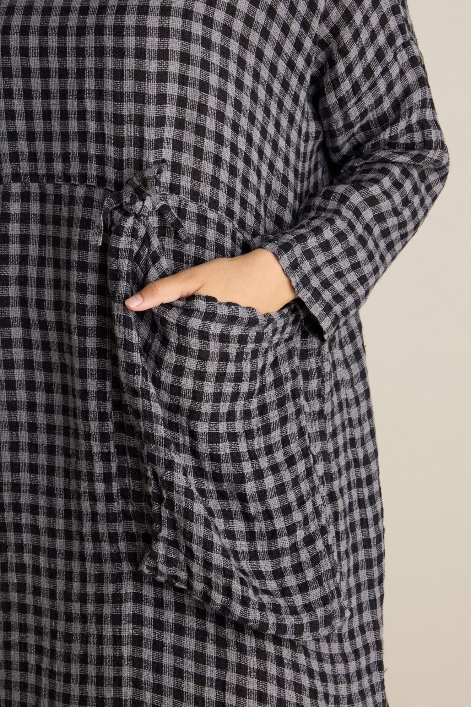 A person wearing a Linen Check Big Pocket Dress in black and white checkered soft linen, with one hand placed in an oversized feature pocket.