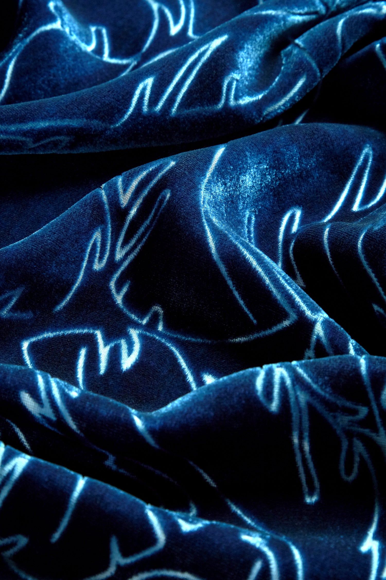 Close-up of a dark blue velvet fabric with a vine devoré design, showcasing shimmering, wavy, embroidered patterns that catch the light. Perfect for transitioning from day to evening wear, this elegant texture adds sophistication to any Vine Devore Dress.