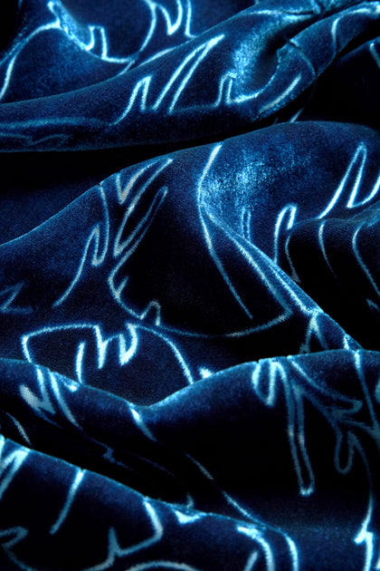 Close-up of a dark blue velvet fabric with a vine devoré design, showcasing shimmering, wavy, embroidered patterns that catch the light. Perfect for transitioning from day to evening wear, this elegant texture adds sophistication to any Vine Devore Dress.