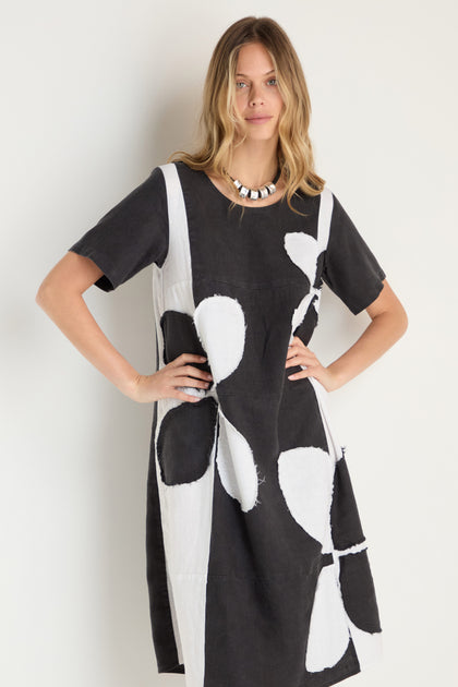 A woman models the Quant Monochrome Linen Dress, a loose-fitting piece featuring large abstract shapes, standing with hands on hips against a plain light background.