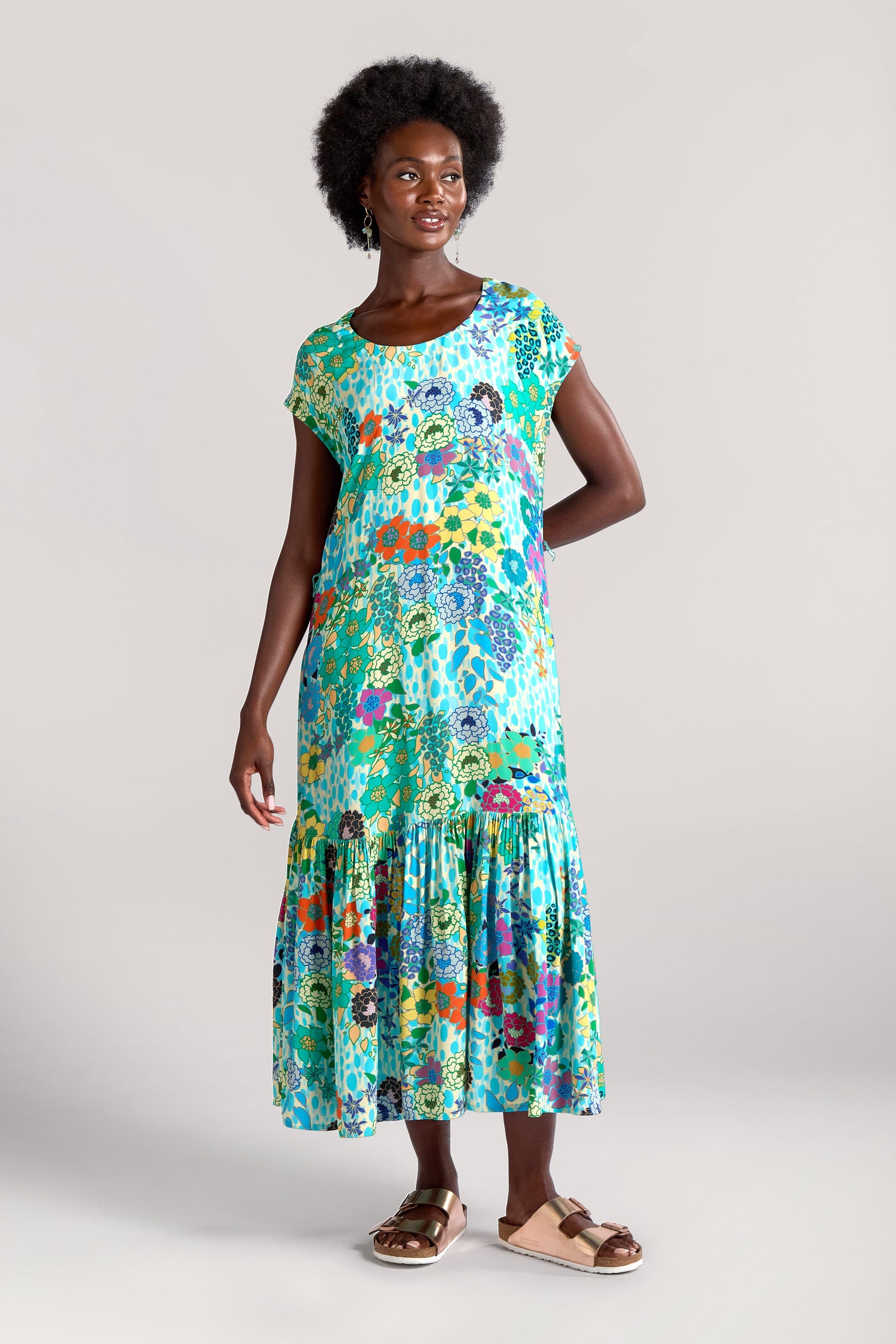 A woman is wearing a Garden Spot Frill Hem Maxi Dress with short sleeves and sandals. The Garden Spot Frill Hem Maxi Dress features a charming design, and she is standing on a plain background.