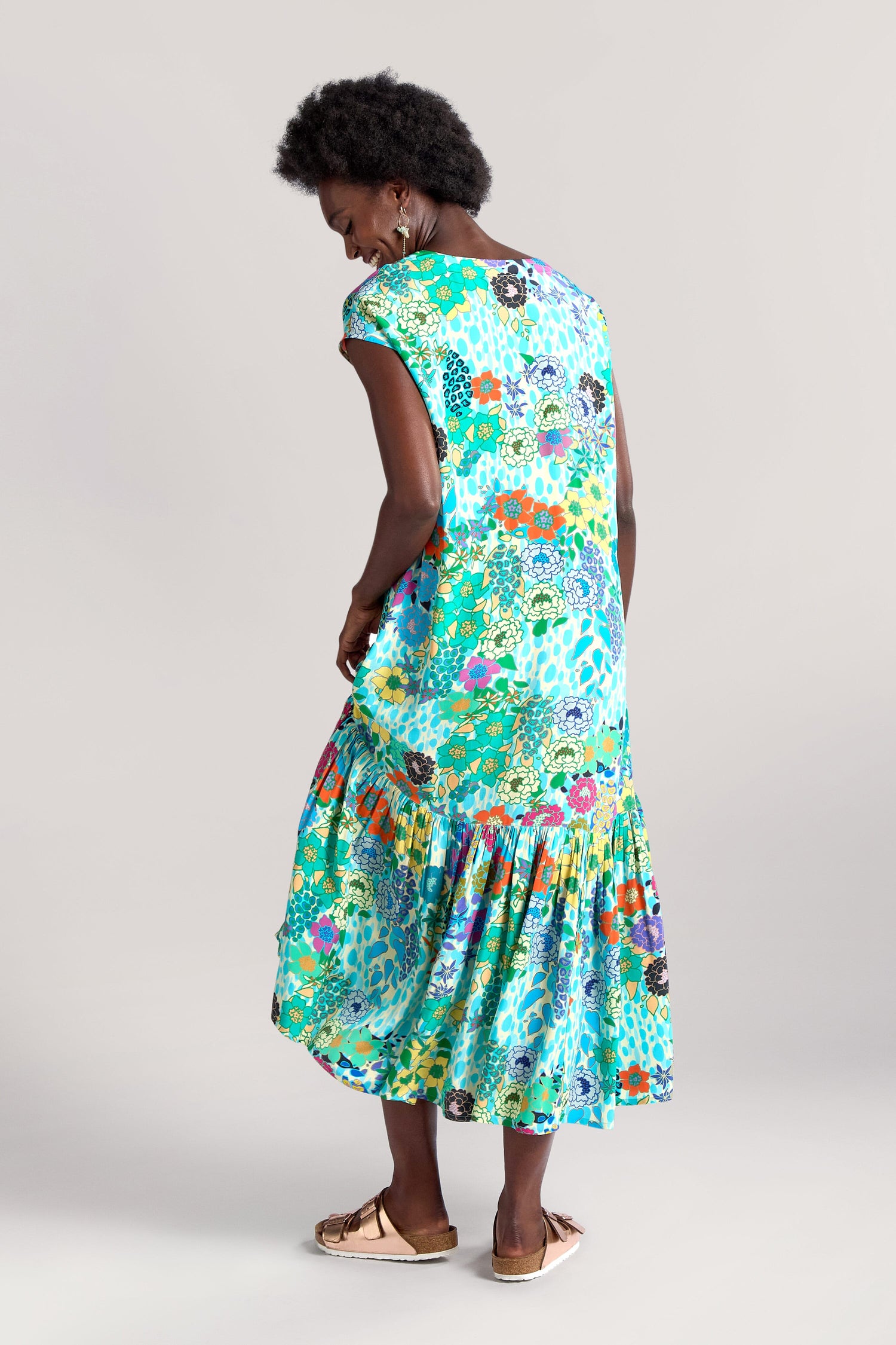 A person wearing a vibrant, Garden Spot Frill Hem Maxi Dress stands with their back to the camera and looks over their shoulder.