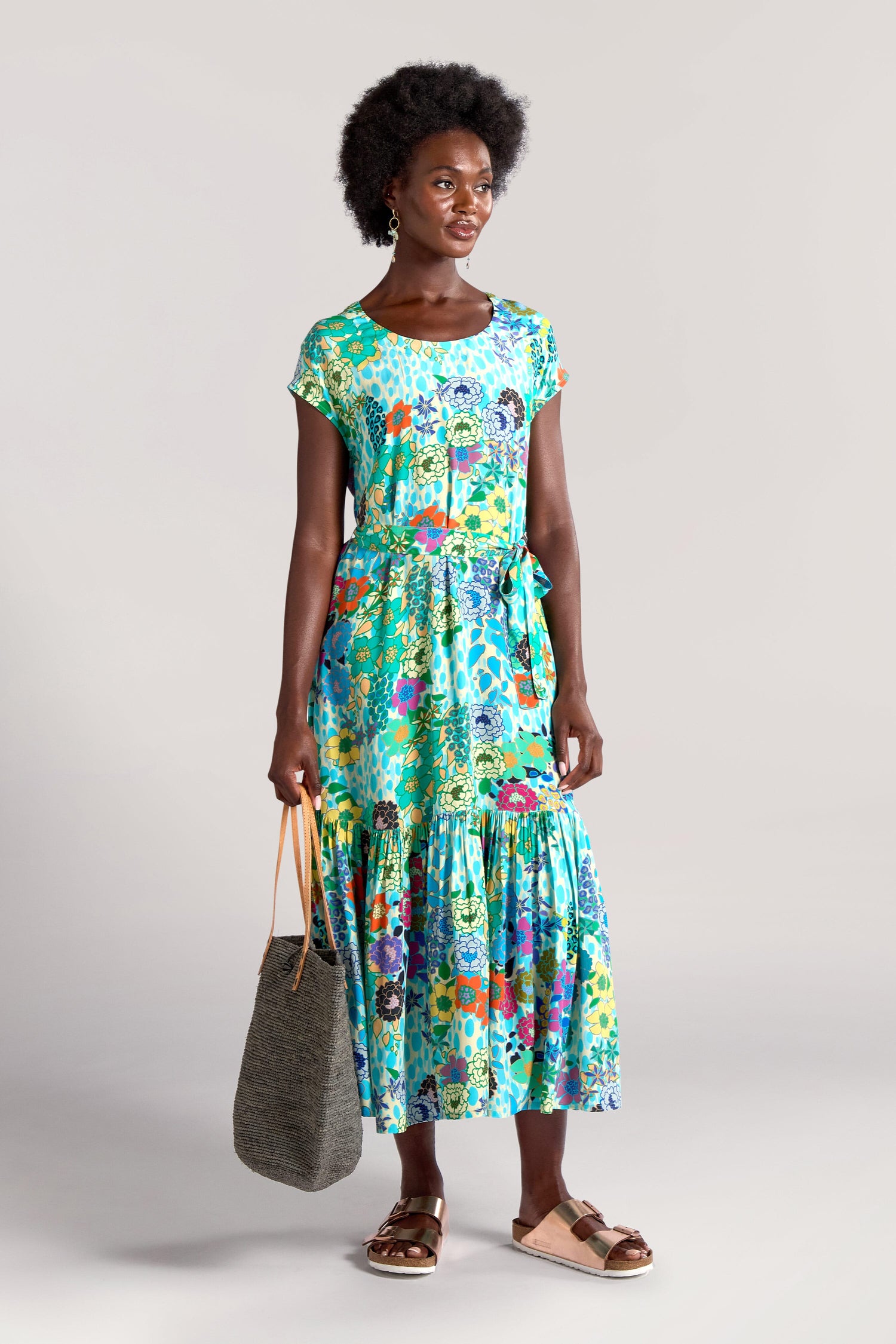 A person stands against a neutral background wearing a Garden Spot Frill Hem Maxi Dress and sandals, holding a grey tote bag.