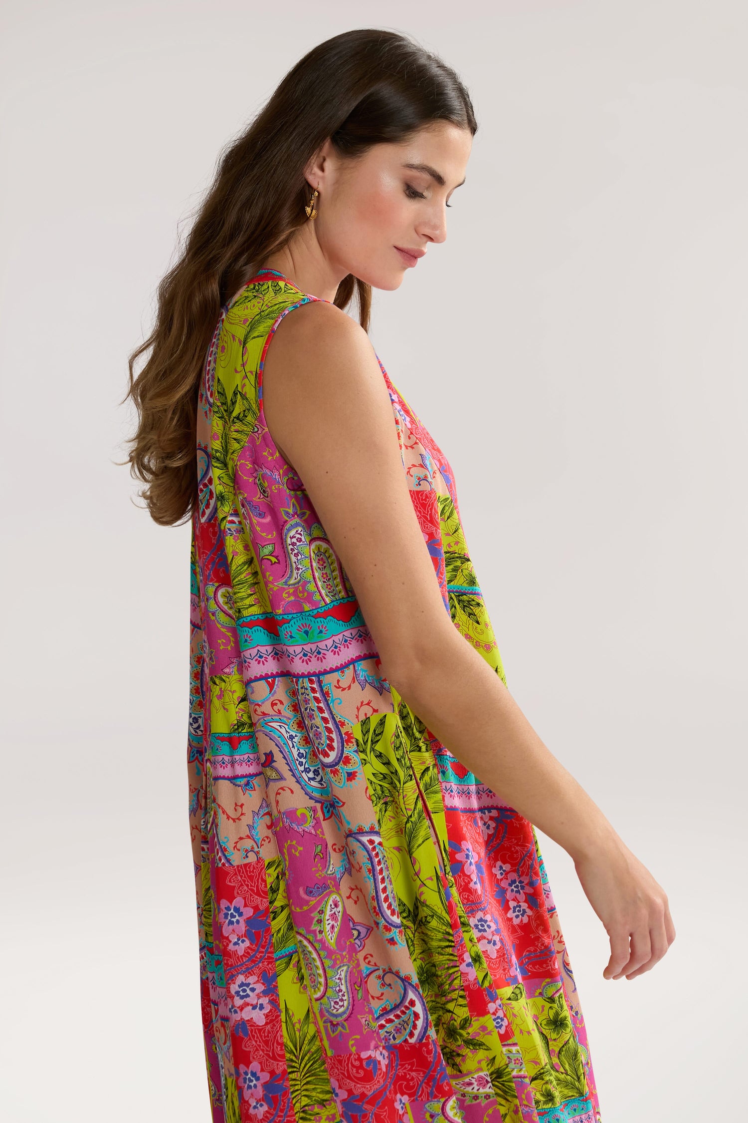 A woman with long brown hair wearing a Tropical Patchwork Sleeveless Bubble Dress stands against a plain background, looking down to one side.