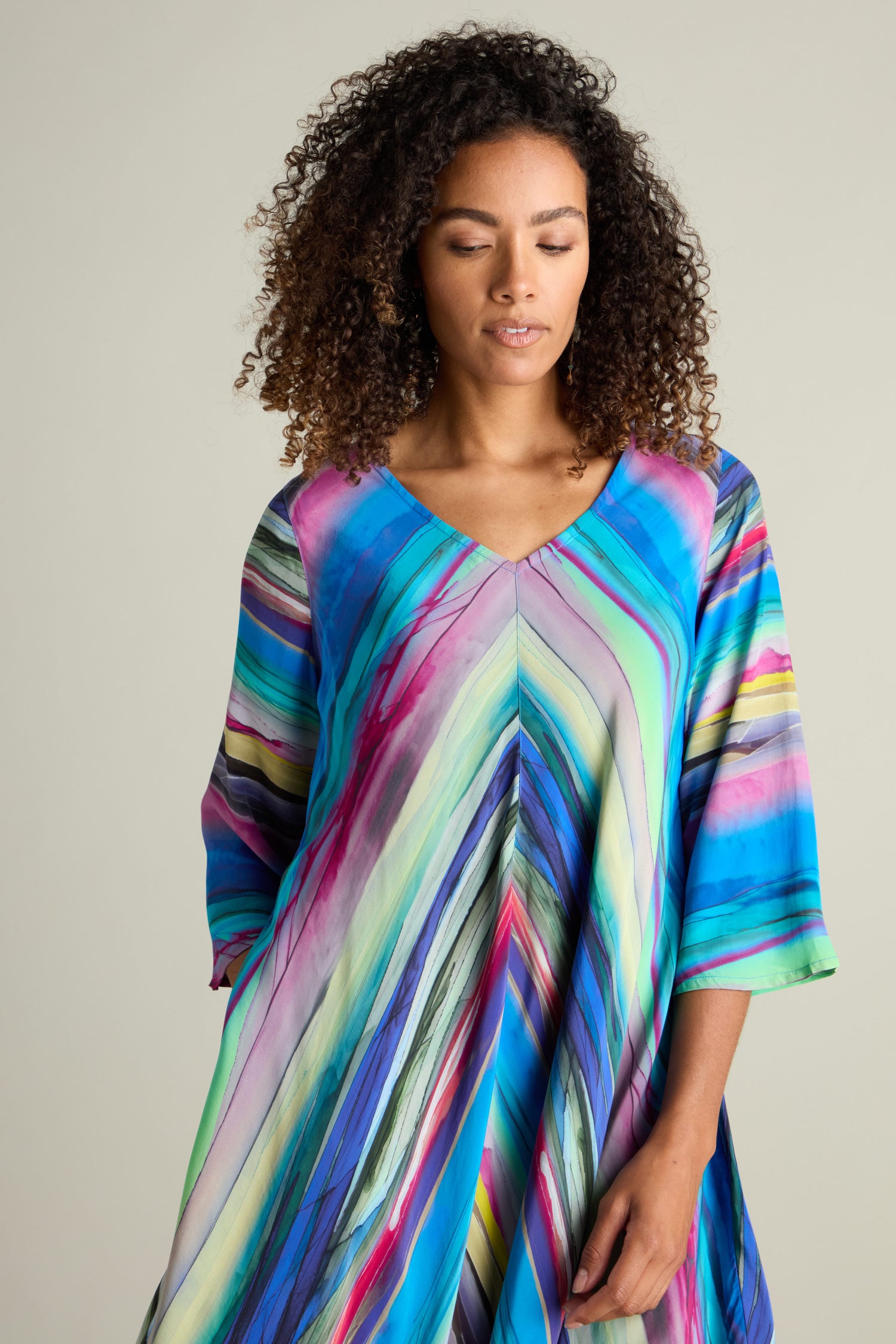 A person with curly hair is wearing the Watercolour Landscape Bubble Dress, made of lightweight viscose fabric, with a calm expression and eyes closed, standing against a plain background.