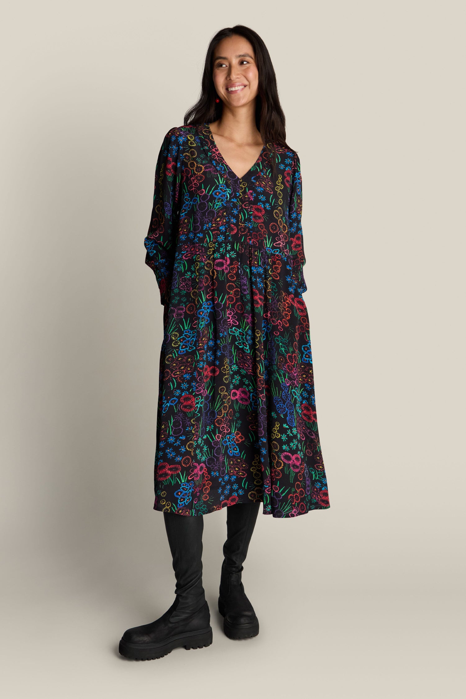 A person stands against a plain background wearing the Embroidered Floral Print Dress paired with black boots.