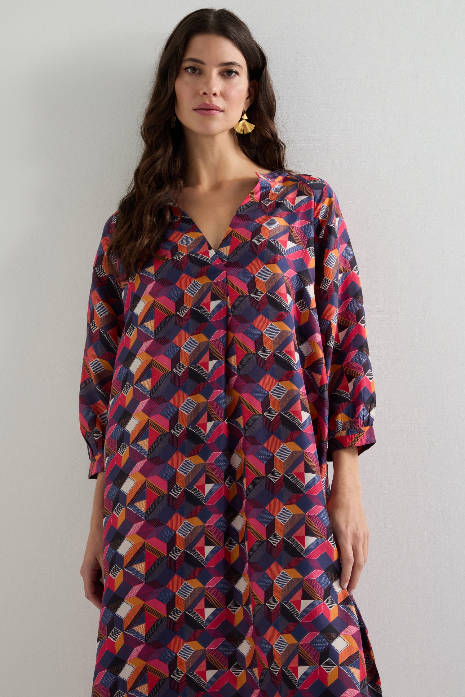 A woman wearing the Small Stitched Squares Silk Dress, featuring a colorful geometric print, relaxed fit, and three-quarter sleeves, stands against a plain background.