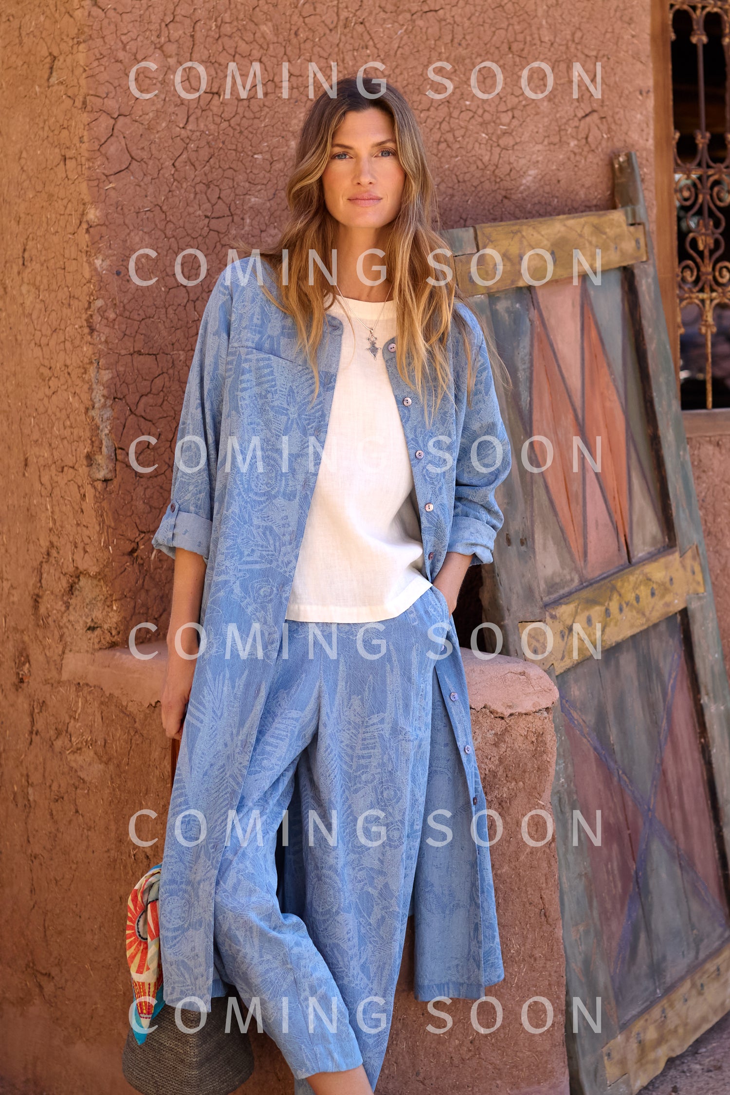 A woman stands against a textured wall in the Floral Jacquard Cotton Shirt Dress over a white top, next to a wooden door. "COMING SOON" is overlaid on the image.