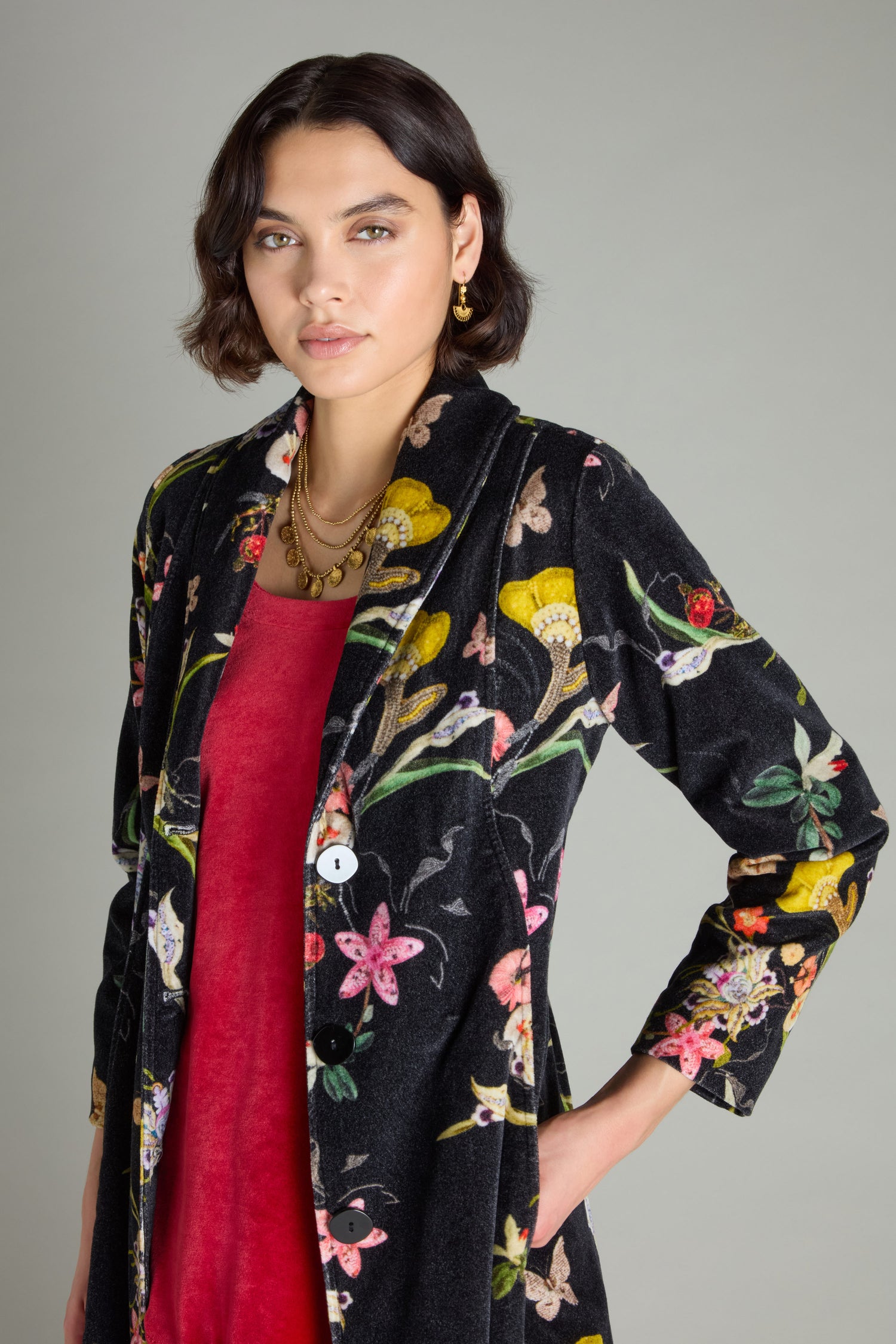 A person wearing the Velvet Vintage Floral Coat with a shawl collar over a red dress stands against a plain background, showcasing an elegant fit-and-flare silhouette.