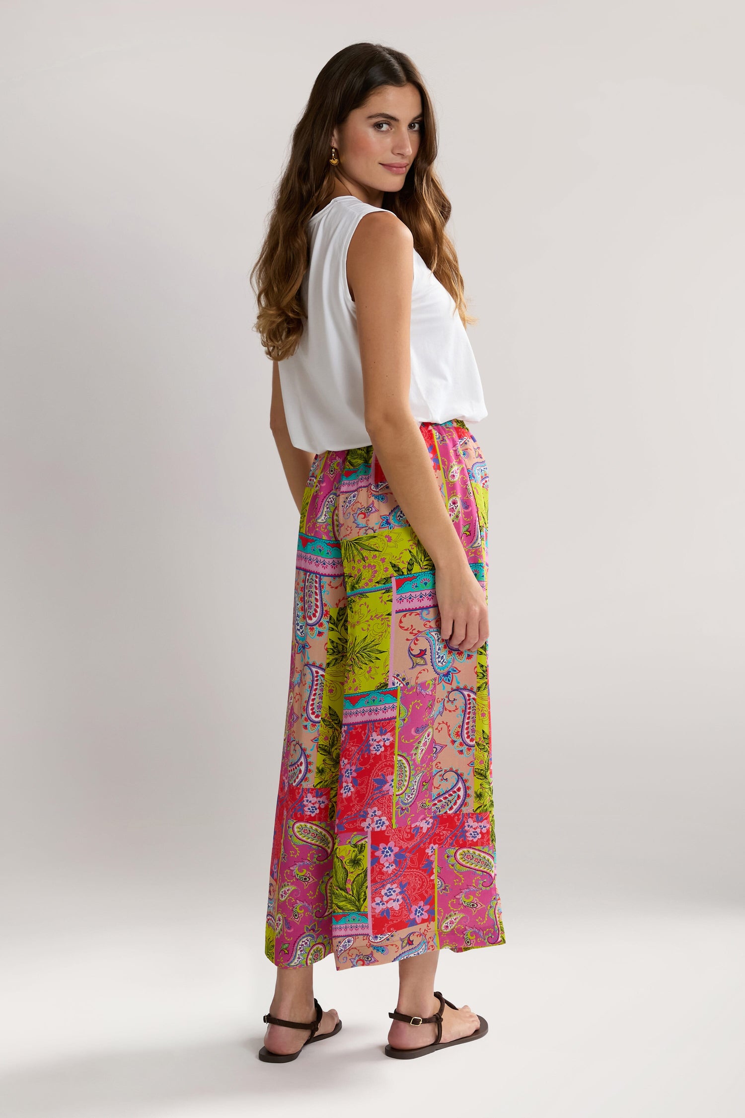 A woman with long hair wears a white sleeveless top and Tropical Patchwork Wide Trouser, standing on a plain background.