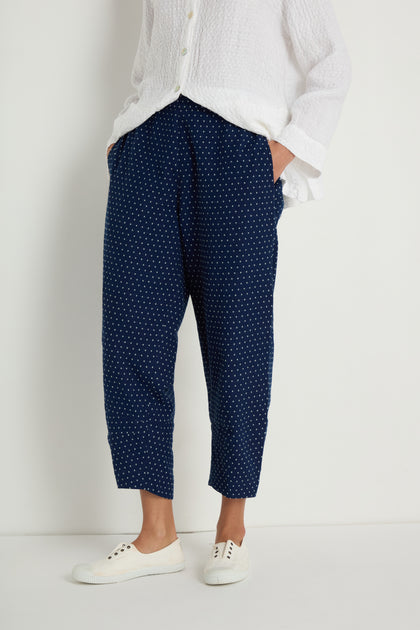 A person wearing a white textured shirt, Indigo Spot Cotton Bubble Trouser with an elasticated waist, and white sneakers stands against a plain white background.