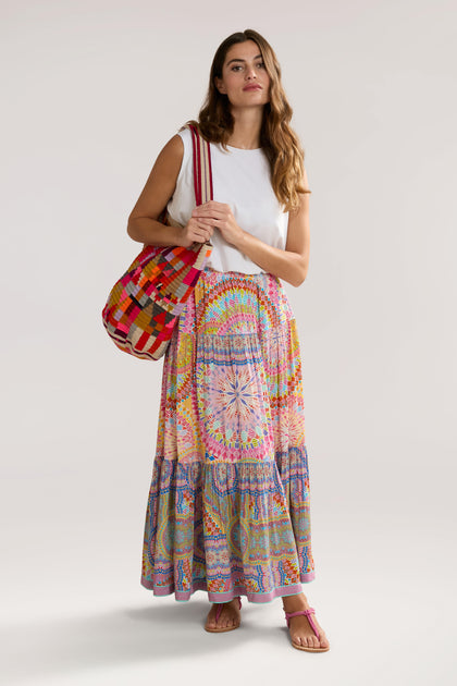 A woman stands holding a red checkered bag, wearing a white sleeveless top, a Circle Mandala Print Skirt with an elasticated waist, and pink sandals.