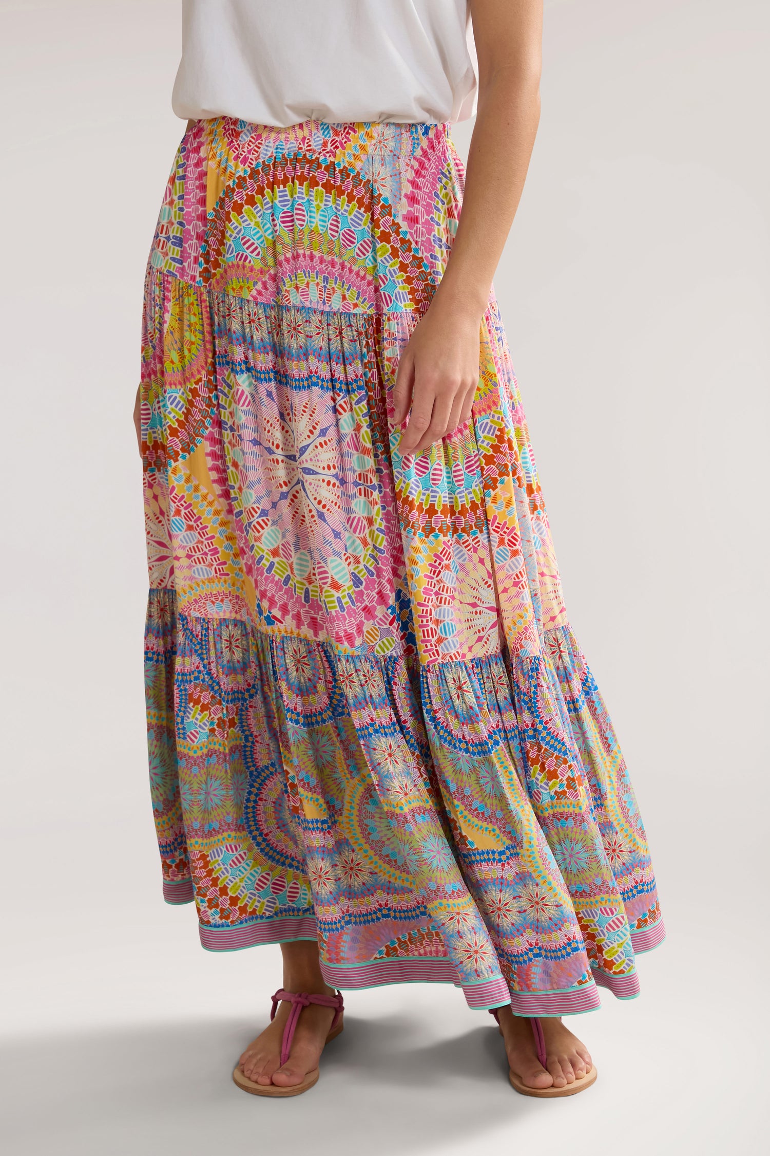 Person wearing a white top and a long, colorful Circle Mandala Print Skirt with an elasticated waist, standing with one hand resting on the Circle Mandala Print Skirt.