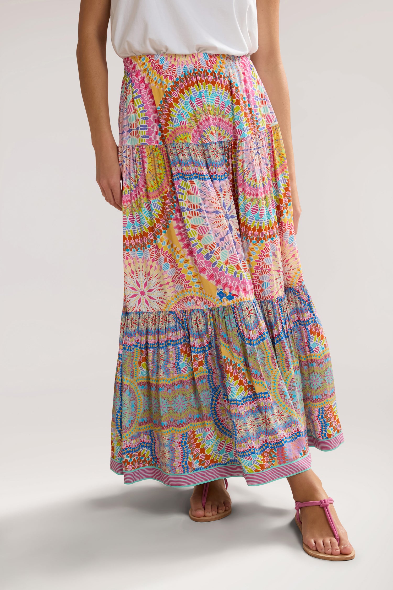 Person wearing a white top and a brightly colored, Circle Mandala Print Skirt with an elasticated waist, paired with pink sandals.