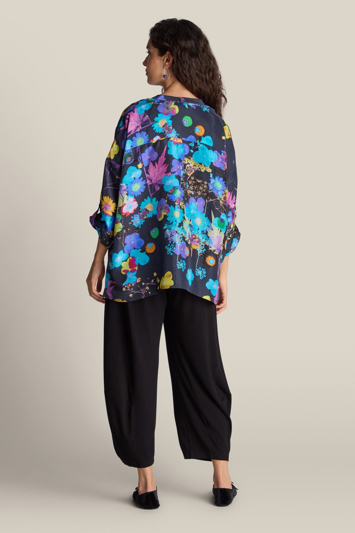 A person with long dark hair is facing away, wearing a Blue Bouquet Silk Shirt and loose black pants.