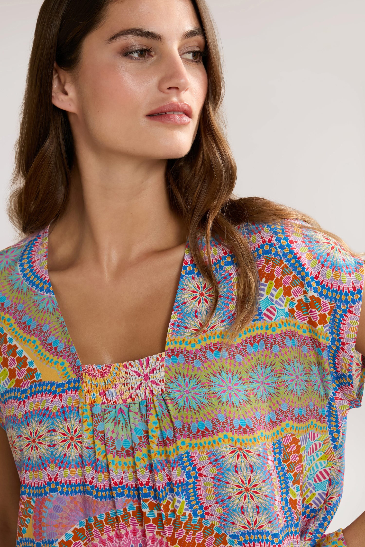 A woman with long, wavy hair wearing a colorful Circle Mandala Print Top looks off to the side against a plain background.