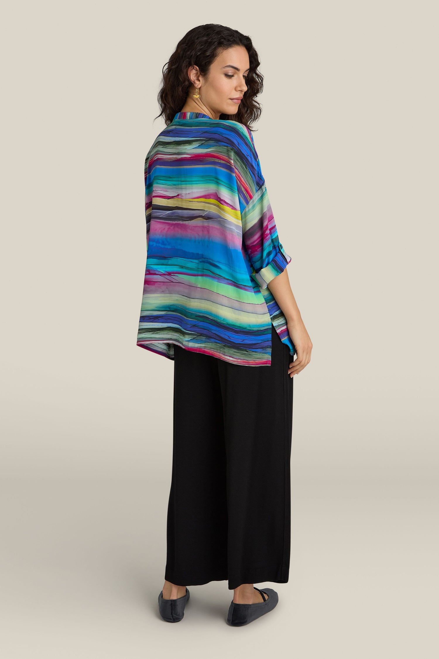 A woman stands sideways wearing the Watercolour Landscape Boxy Shirt and black wide-leg pants, looking over her shoulder.