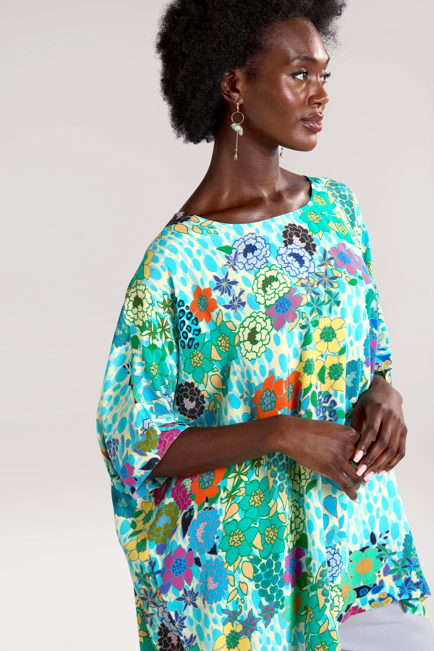 A person wearing a colorful Garden Spot Tunic and dangling earrings, standing against a plain background.