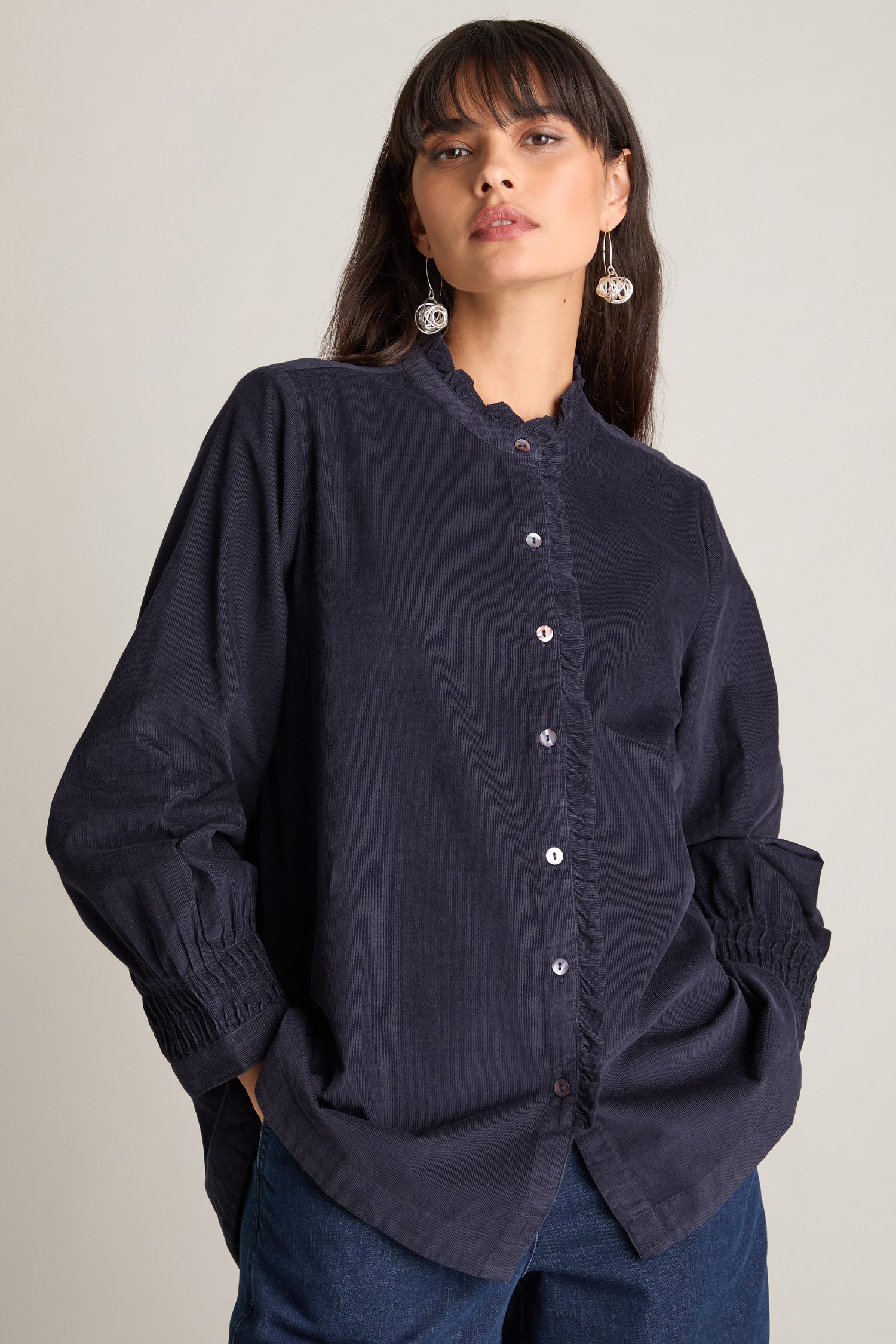 A person wearing a dark, long-sleeved Pinwale Cord Pleat Frill Placket Shirt and jeans stands against a plain background.