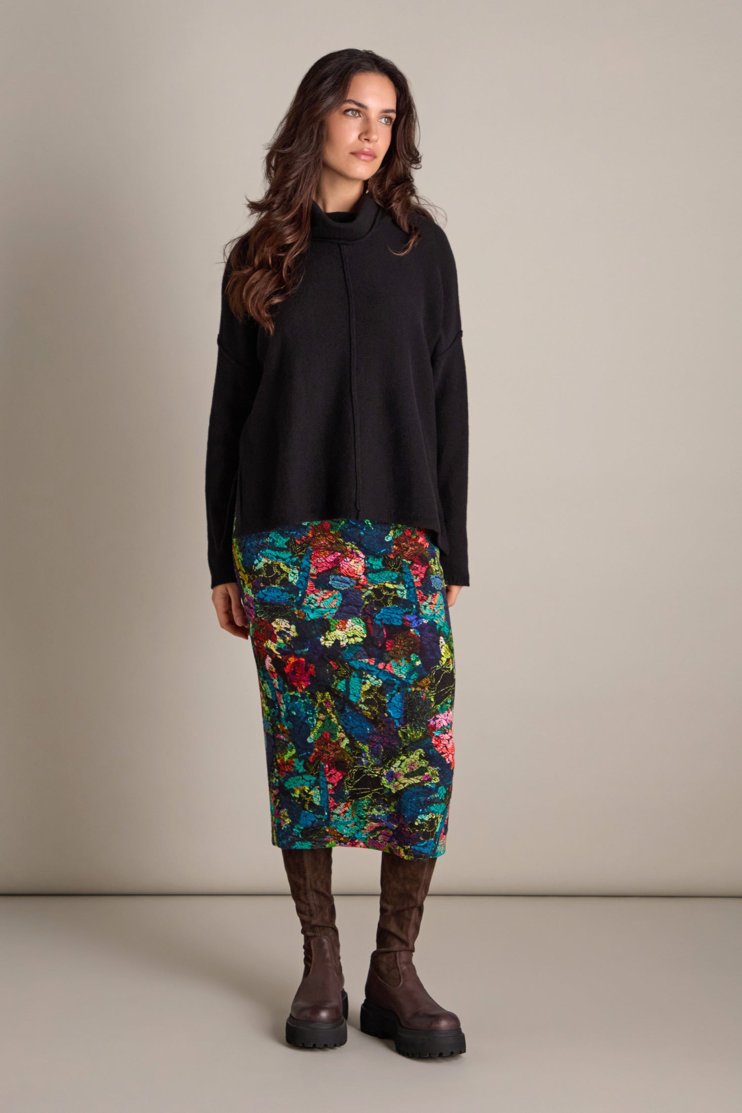 A person wearing a black sweater, the Abstract Floral Jersey Tube Skirt exuding artistic elegance, and brown boots stands against a plain background.