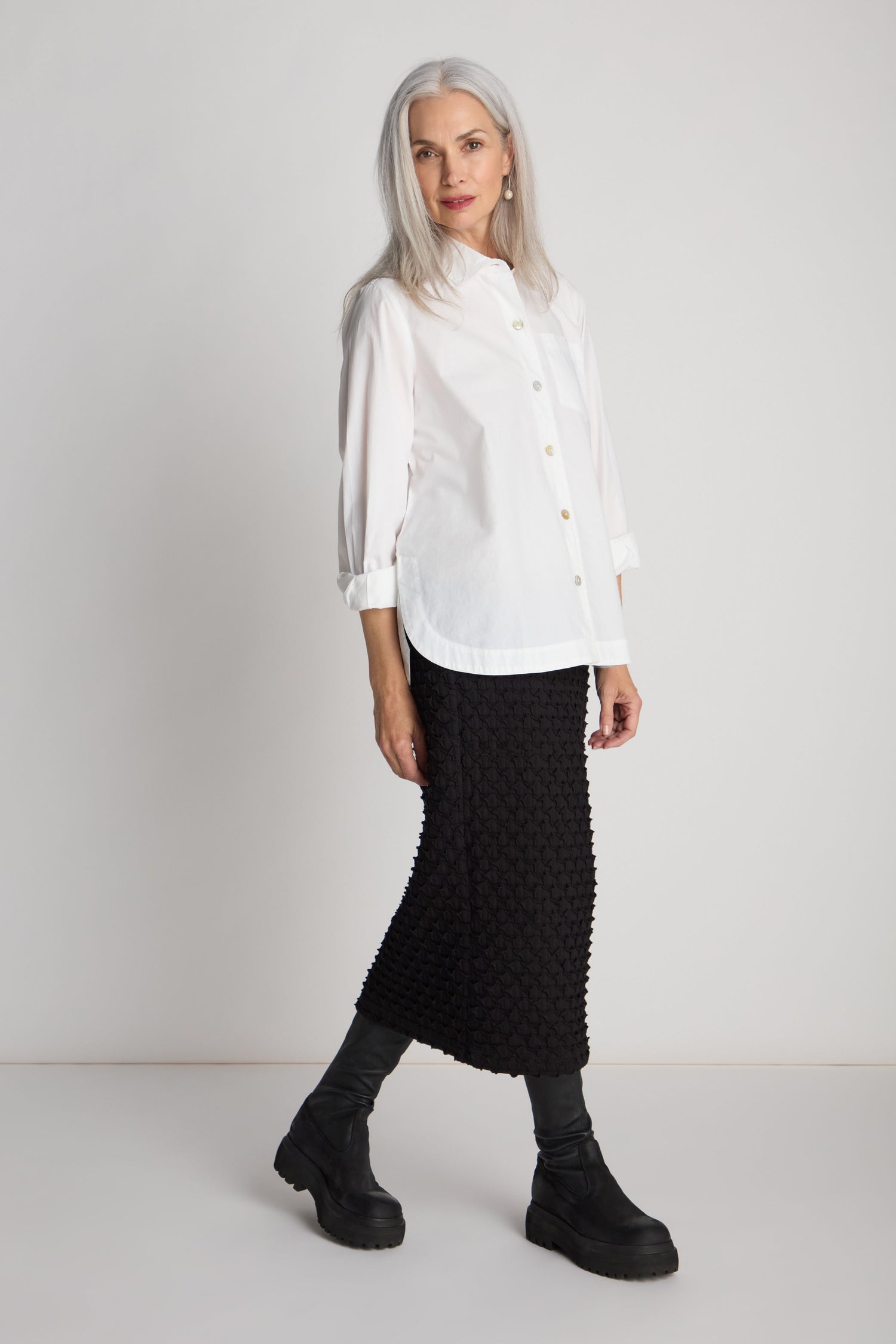 A woman with long gray hair wearing a white button-up shirt, a Pocket Jersey Tube Skirt with an elasticated waist, and black boots stands against a plain white background.