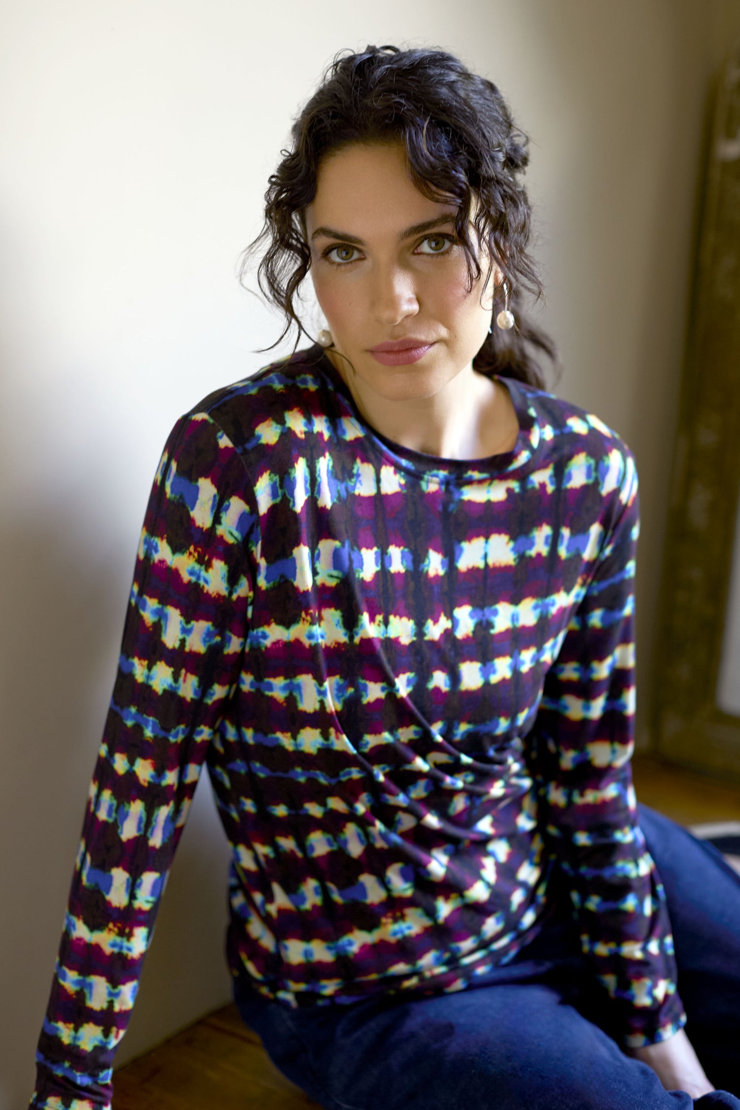 A person with long, dark curly hair wearing a Marble Stripe Jersey Top sits indoors, looking at the camera.