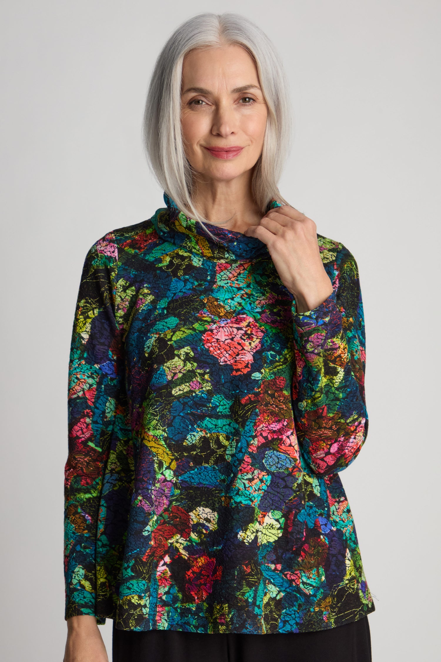 A woman with long gray hair is wearing an Abstract Floral Jersey Cowl Neck Top and black pants, standing against a neutral background.