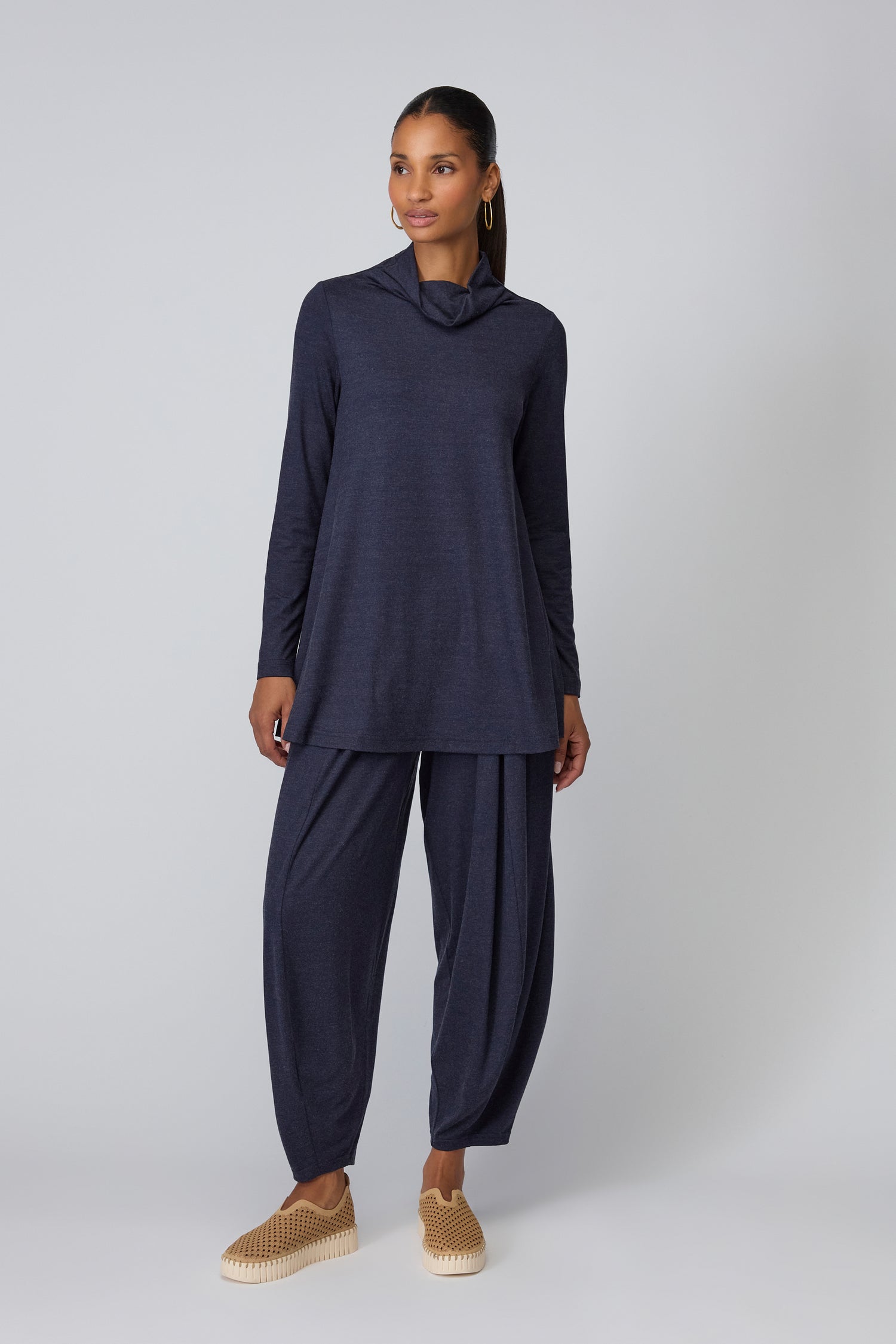 A woman stands against a plain background wearing a long-sleeved dark blue tunic, matching loose pants, and Latte Tulip Platform Slip On Shoes featuring a recycled microfibre upper.