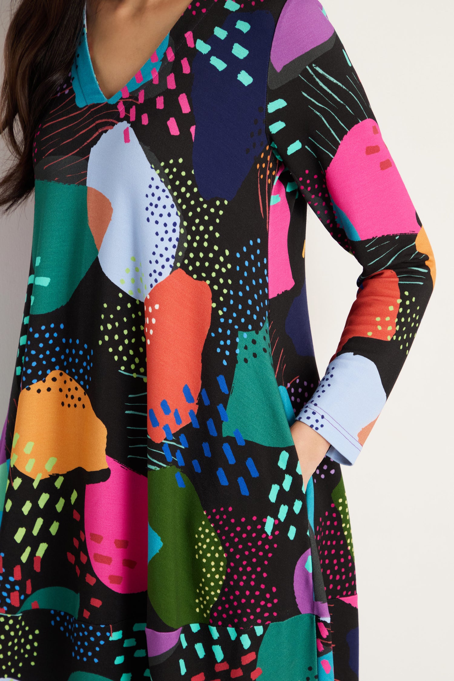 A person wears the Mark Making Print Jersey Bubble Dress, featuring a colorful abstract pattern of various shapes and bright colors on a black background, made in England.