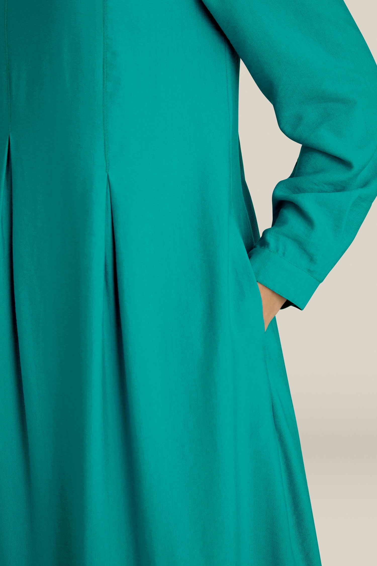 Person wearing a teal Textured Viscose Bubble Dress with pleats and long sleeves, showcasing everyday elegance with their right hand in the pocket.