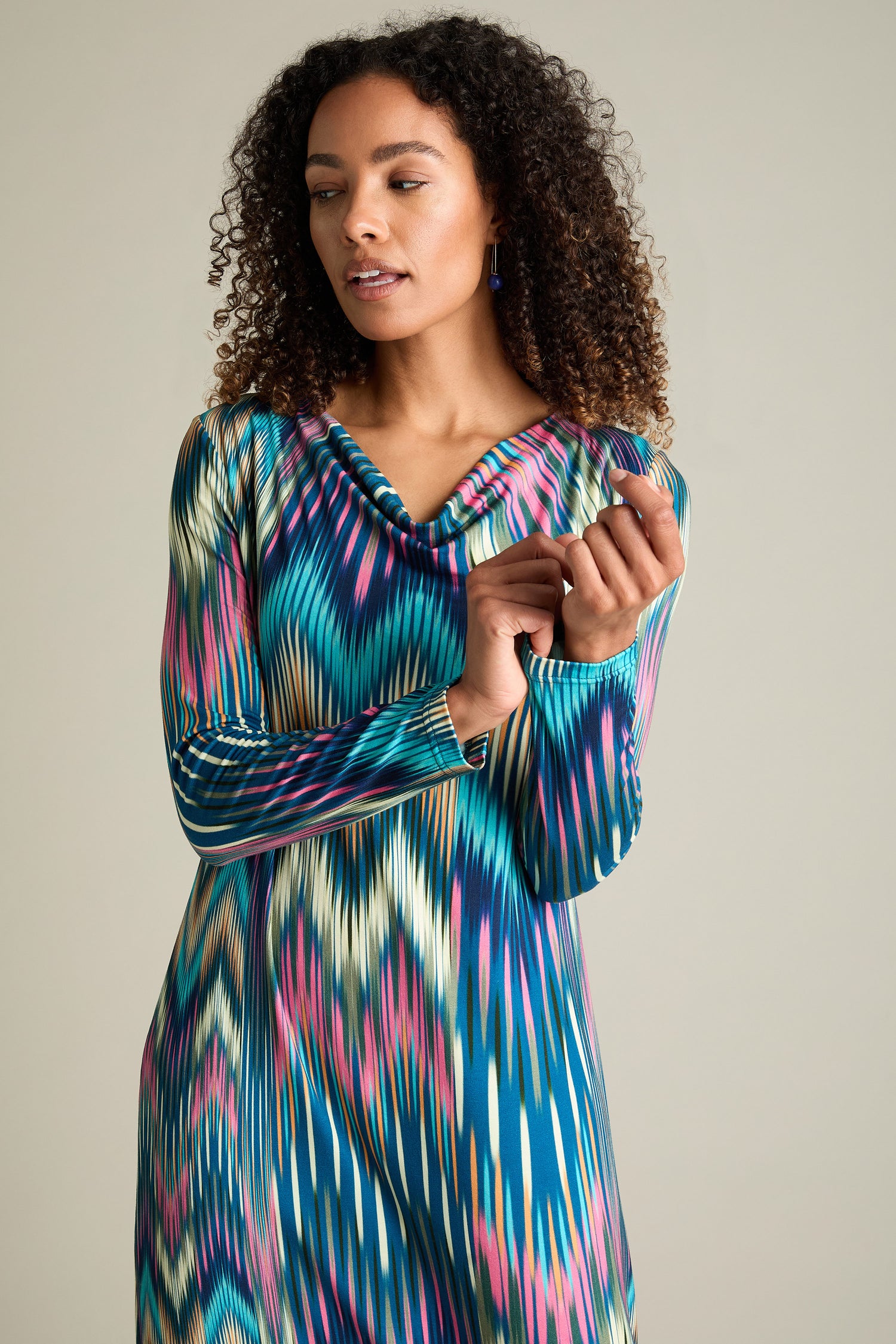 A person with curly hair wearing the Autumnal Ikat Jersey Dress looks down while lightly touching their hand.