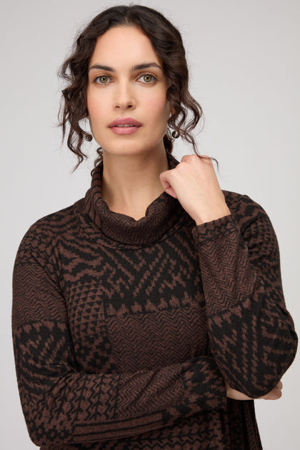 A woman with wavy dark hair wears a Textured Ikat Patchwork Jersey Dress, standing against a plain light background and looking at the camera with a neutral expression.