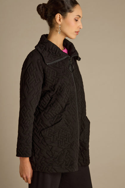 A woman in profile is standing against a beige background, wearing the Abstract Quilted Cotton Jacket with dolman sleeves, crafted from black quilted cotton.