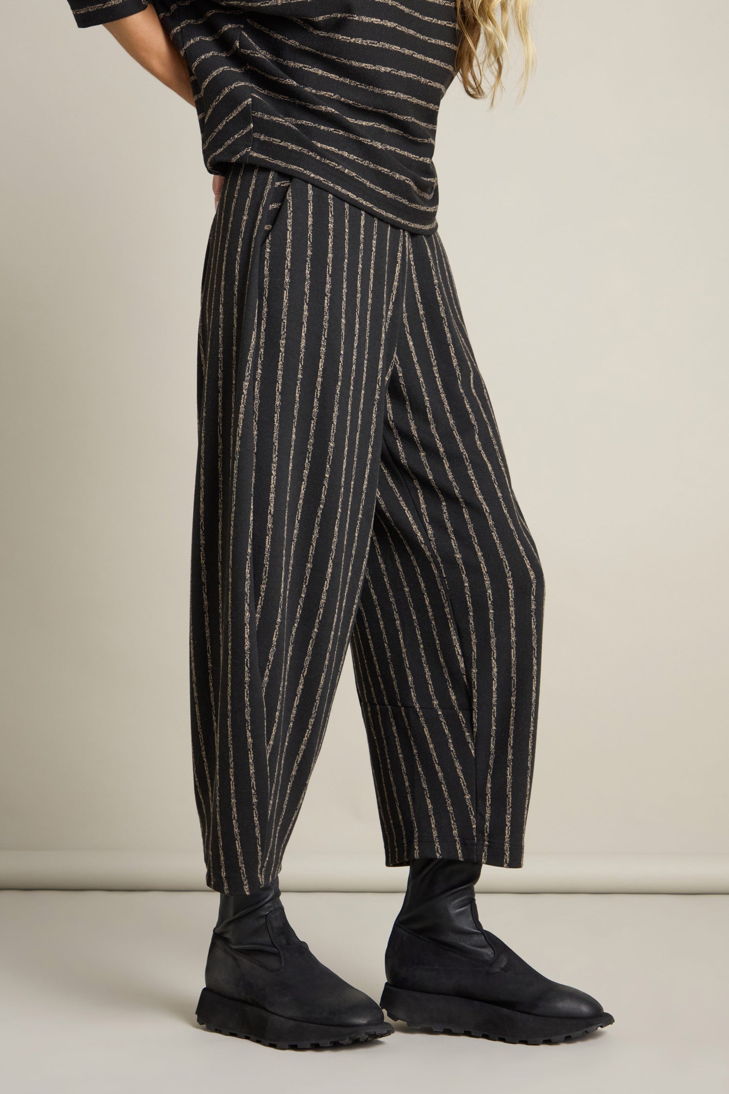 Person wearing the lower half of a stylish outfit featuring the Broken Stripe Jersey Bubble Trouser in black with vertical pinstripes, paired with black footwear, giving the look a modern edge.