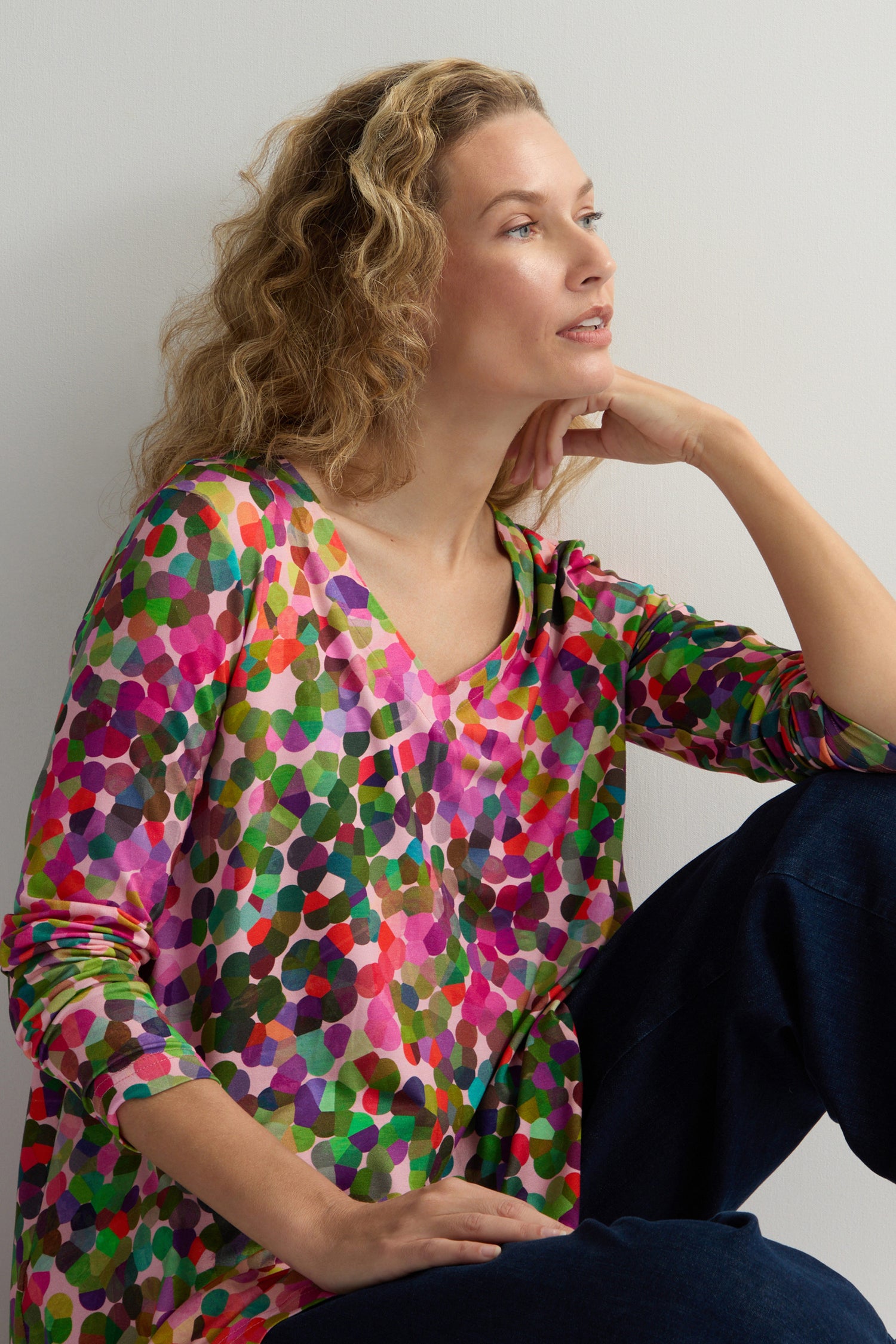 Wearing the Abstract Confetti Jersey Top with a fit-and-flare silhouette and dark pants, a person gazes thoughtfully to the side against a plain backdrop.