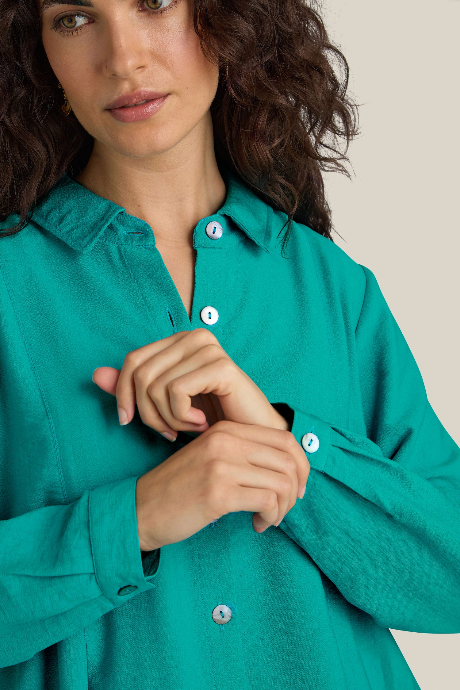 A person wearing a Textured Viscose Pleat Shirt in turquoise blue adjusts their sleeve while looking forward.