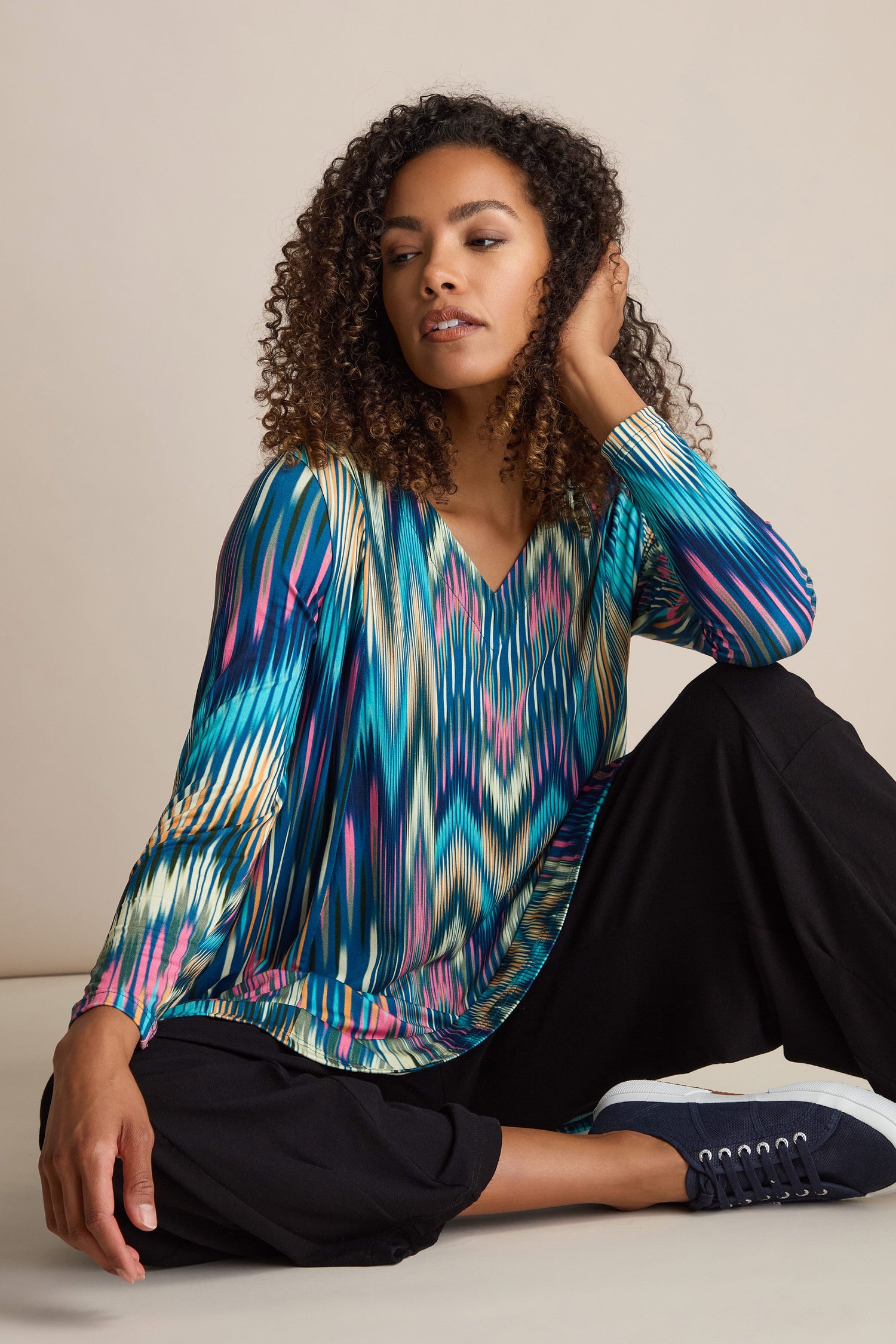 A person sits on the floor with one hand touching their head. They are wearing the Autumnal Ikat Jersey Top, black pants, and navy blue sneakers.