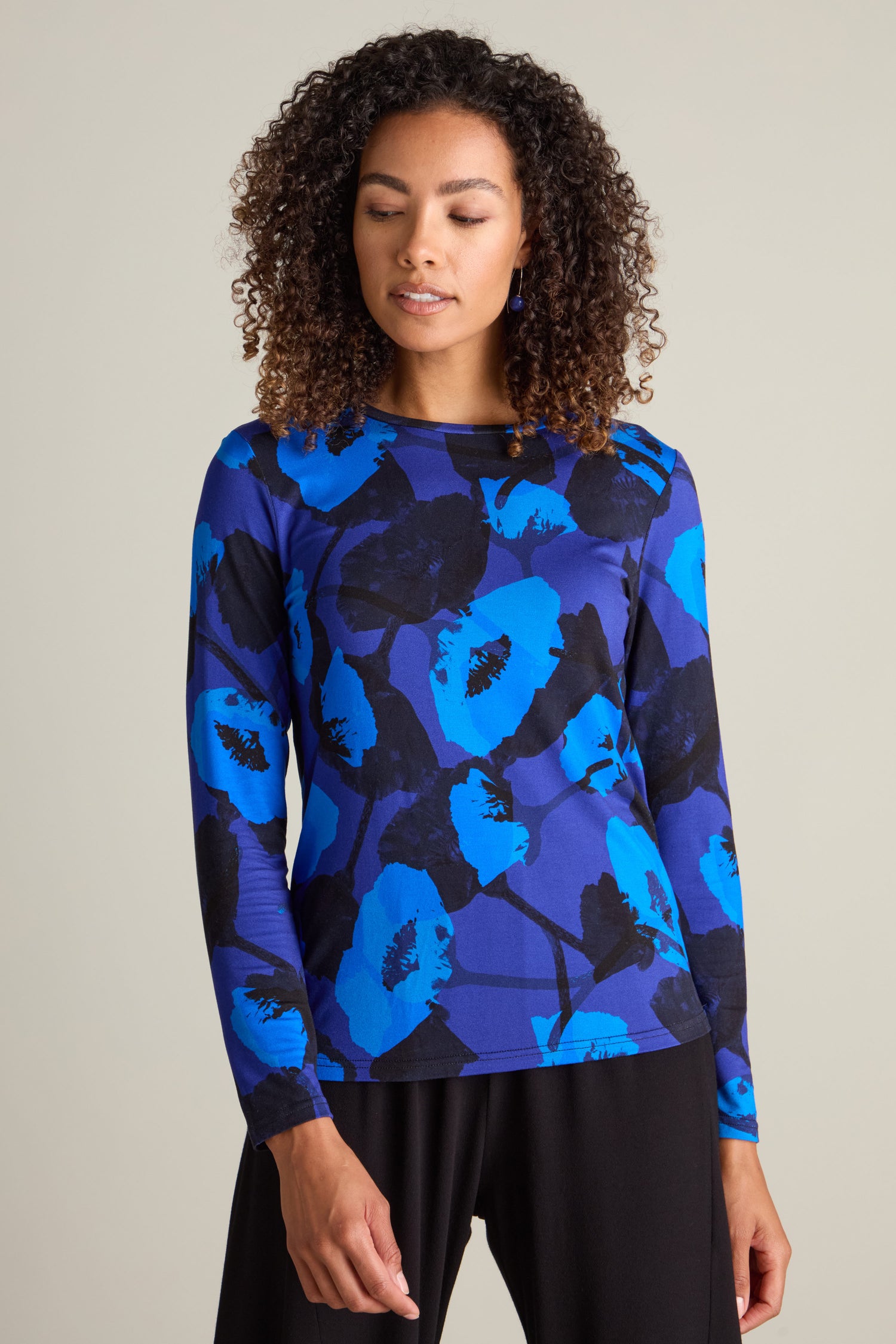 A person with curly hair is wearing a slim-fit, Flowering Poppies Jersey Top.