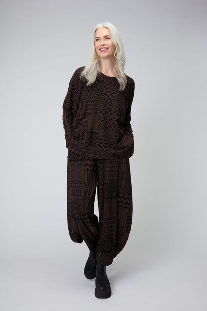 A woman with long gray hair wears the Textured Ikat Patchwork Jersey Top, loose-fitting pants, and black boots while standing against a plain light gray background.