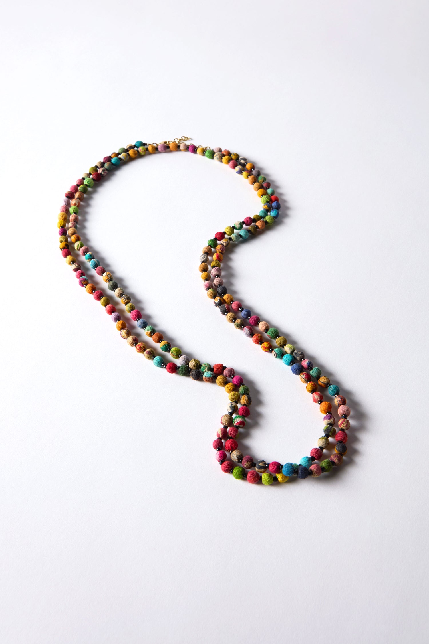 The Kantha Long Bead Spheres Necklace showcases vibrant beads made from upcycled textiles, forming a looping design on a plain white backdrop.