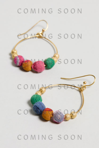 Kantha Gilded Hoop Earrings feature gold hoops adorned with colorful fabric and gold beads, displayed on a light surface. "COMING SOON" is repeated across the image.