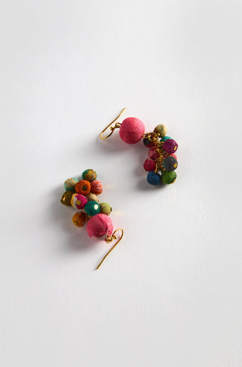 The Kantha Spheres Earrings are vibrant, featuring clusters of multi-colored textile spheres with gold hooks. They are meticulously handcrafted from recycled textiles, set against a white background.